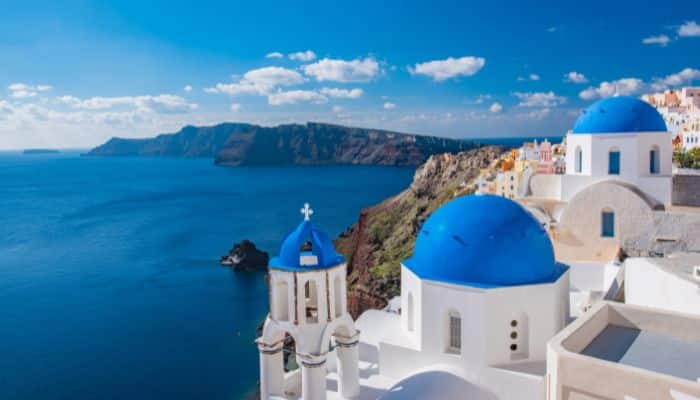 Picture capturing the 3 blue domed buildings in Santorini with a white city and cliffside background