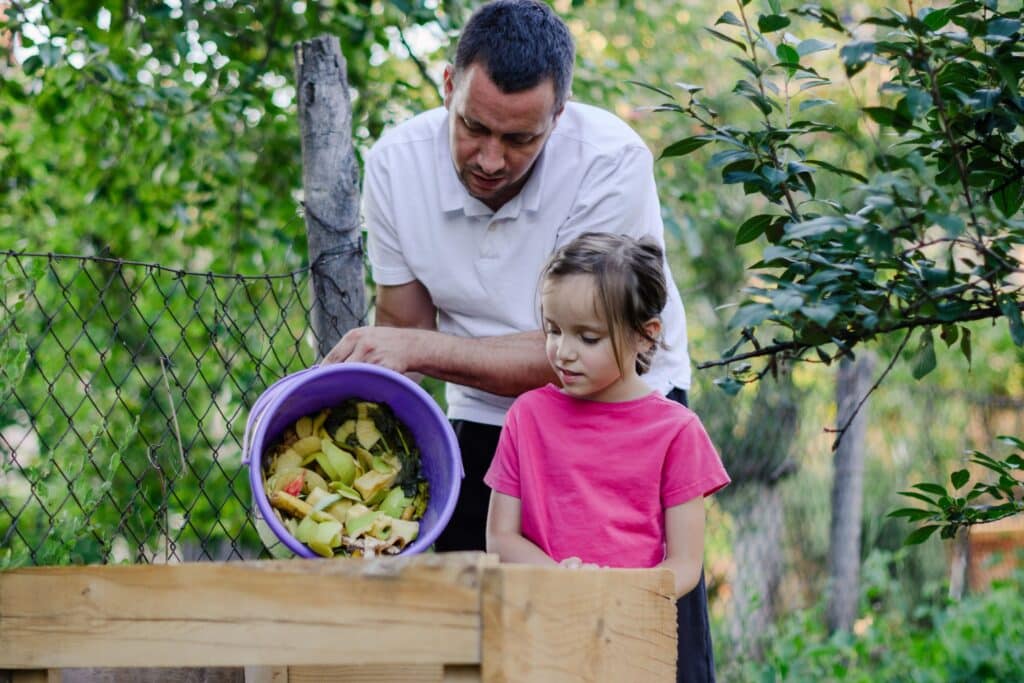Father and daughter emptying a bucket of compost outside