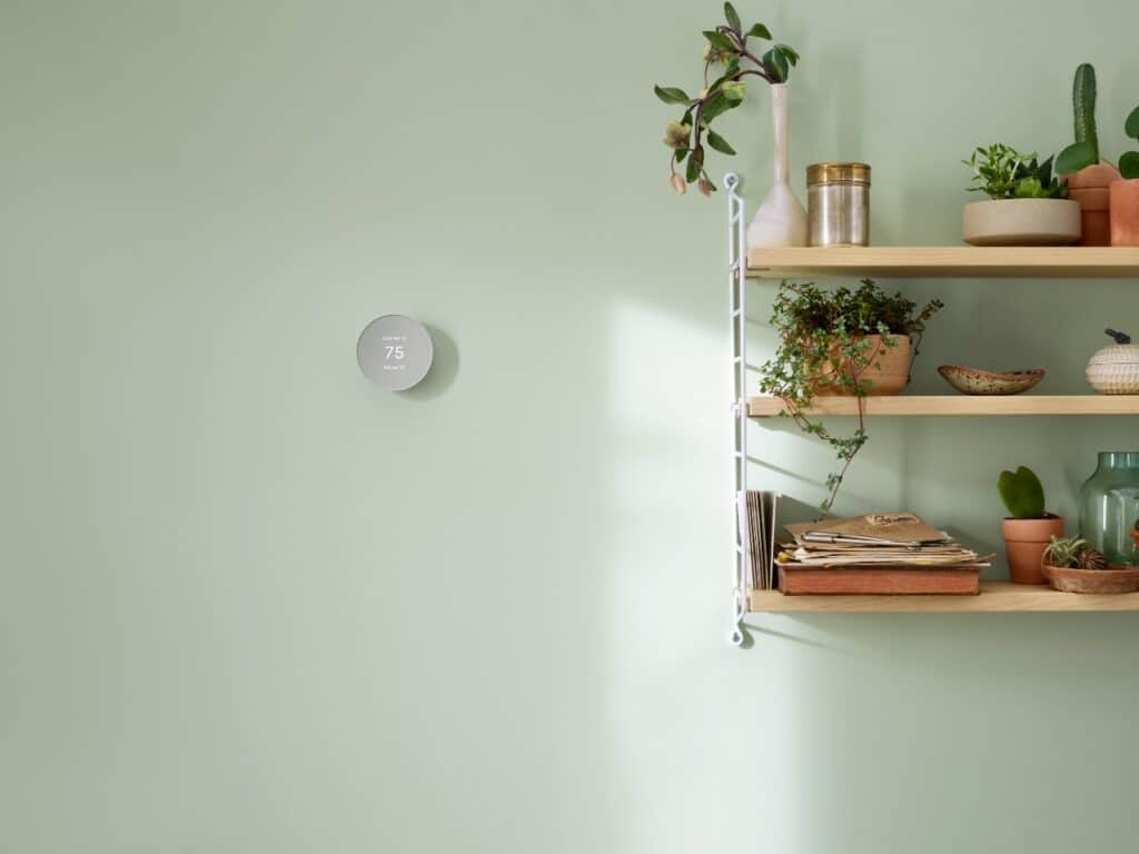 Smart thermostat on the wall with a shelf of plants and pottery beside it