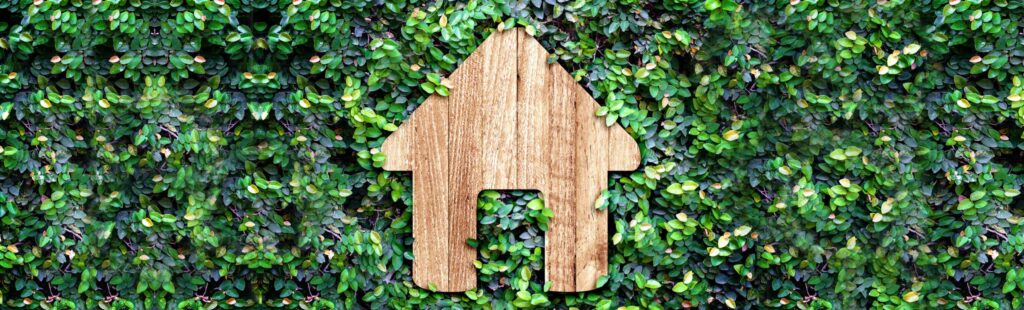Wooden house cutout up against wall of leaves