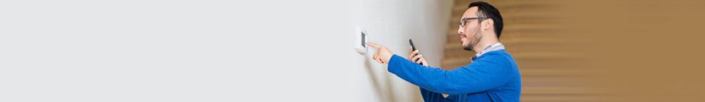 Man holding his phone and interacting with a thermostat on a wall