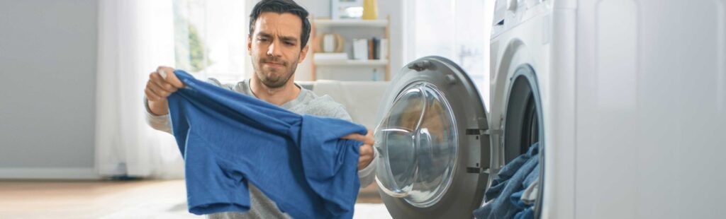 Man standing in front of a washing machine analyzing his freshly washed shirt with a look of disappointment
