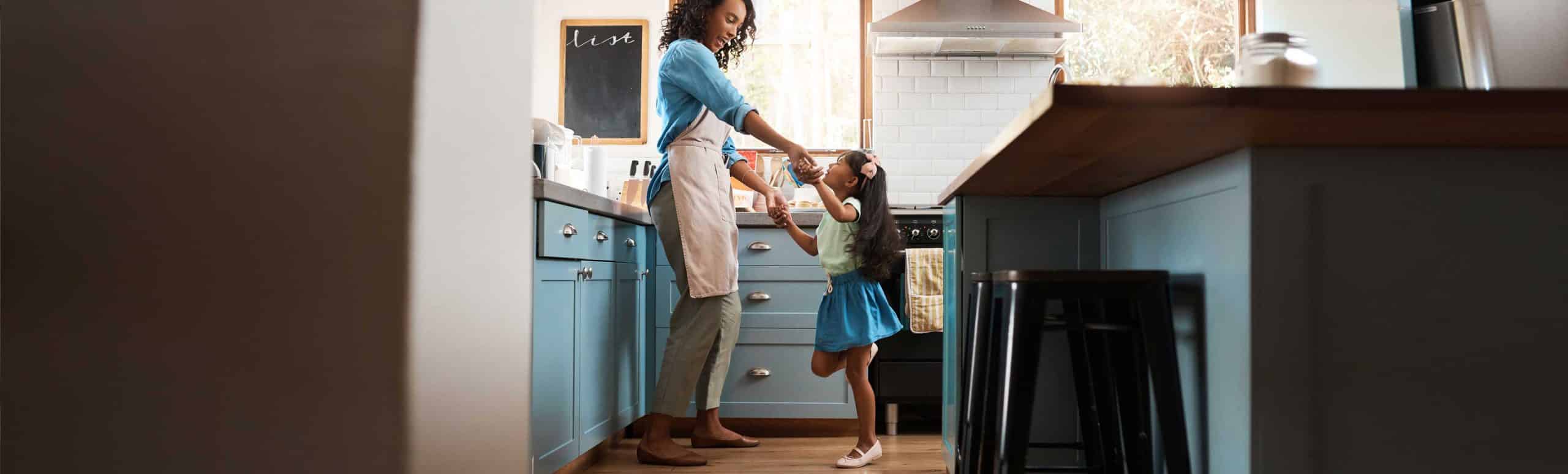 Mother in apron holding hands with her child dancing in the kitchen