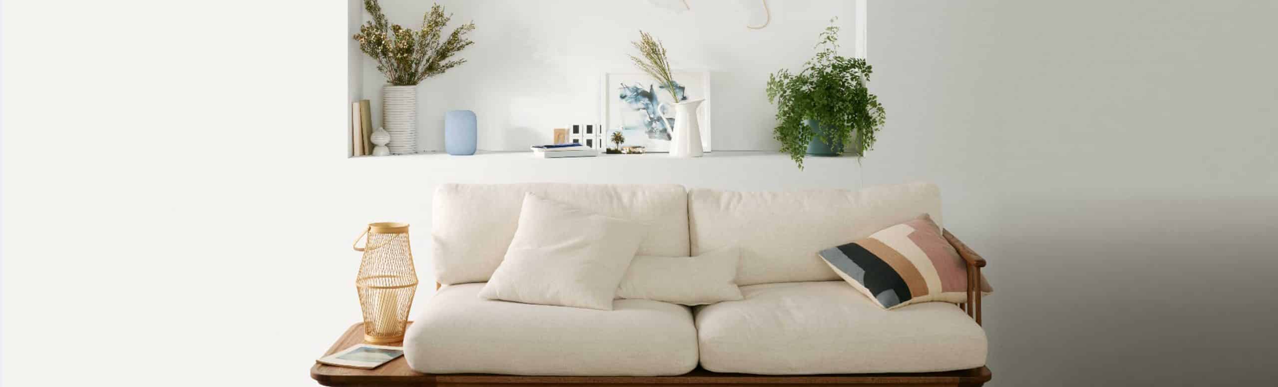 Couch in an open white room with plants and a light blue Google Nest in the back