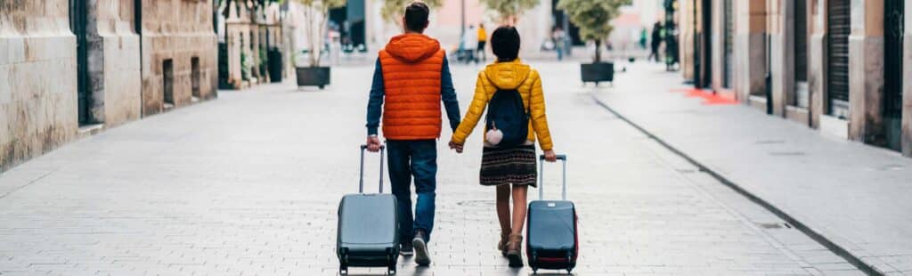 2 people holding hands while rolling a suitcase each down an open walkway