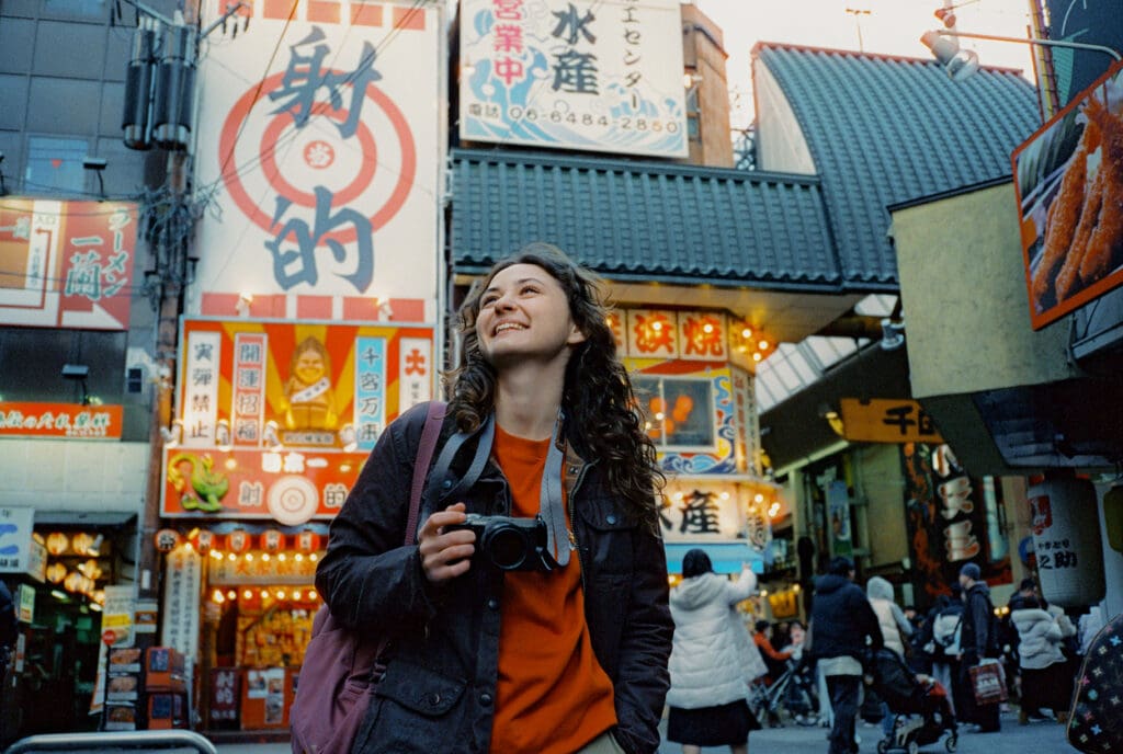 Carefree woman photographing with camera in Osaka during experiential trip to Japan. Shot on camera film