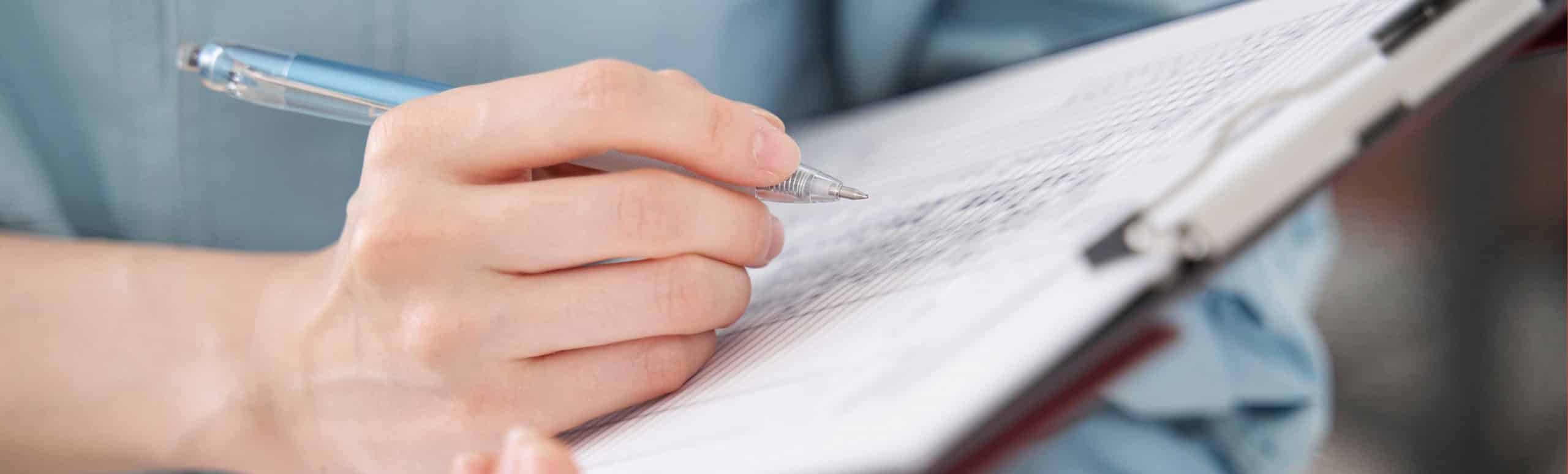 Righthand holding a pen writing on paper attached to clipboard