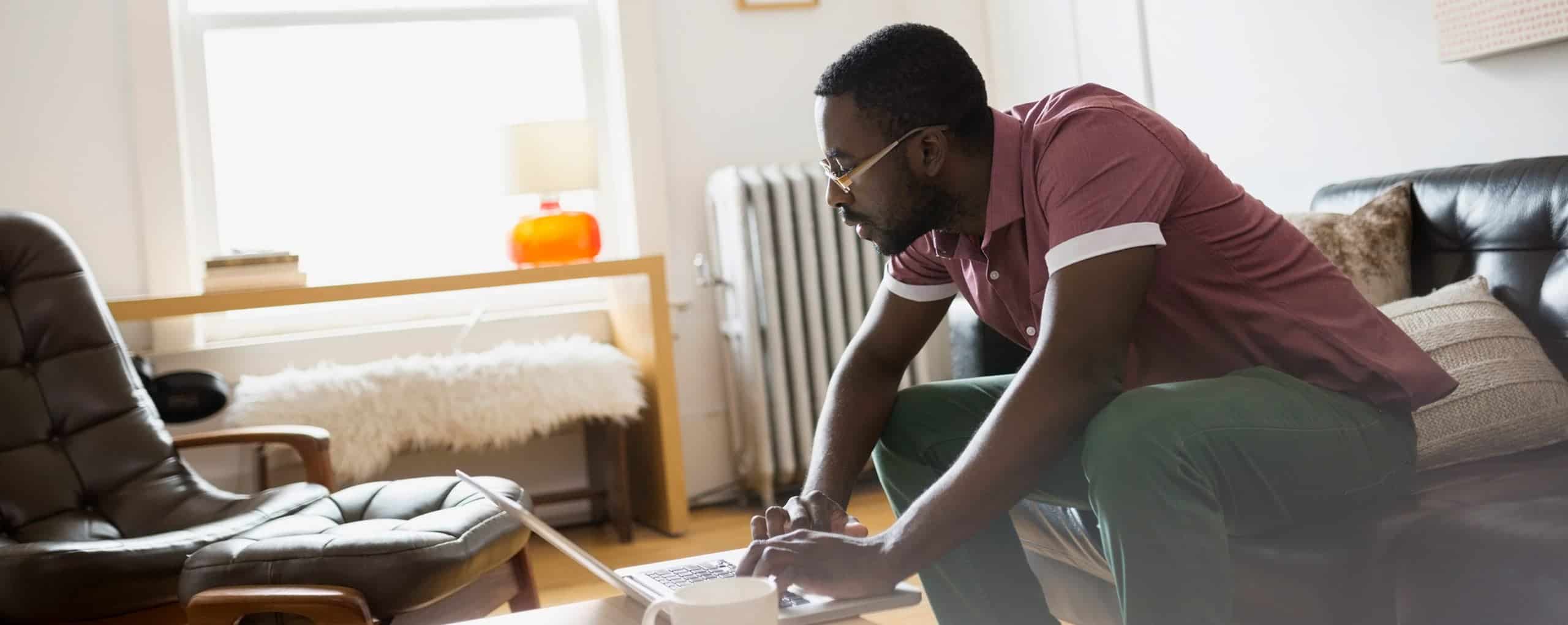 Man sitting on the couch slouching over to coffee table with his computer