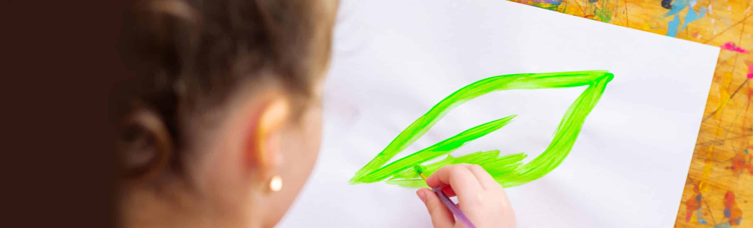 Child painting a green leaf on a white paper