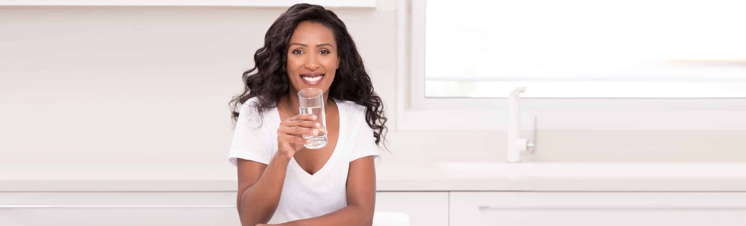 Woman holding up clean cup of water by the kitchen
