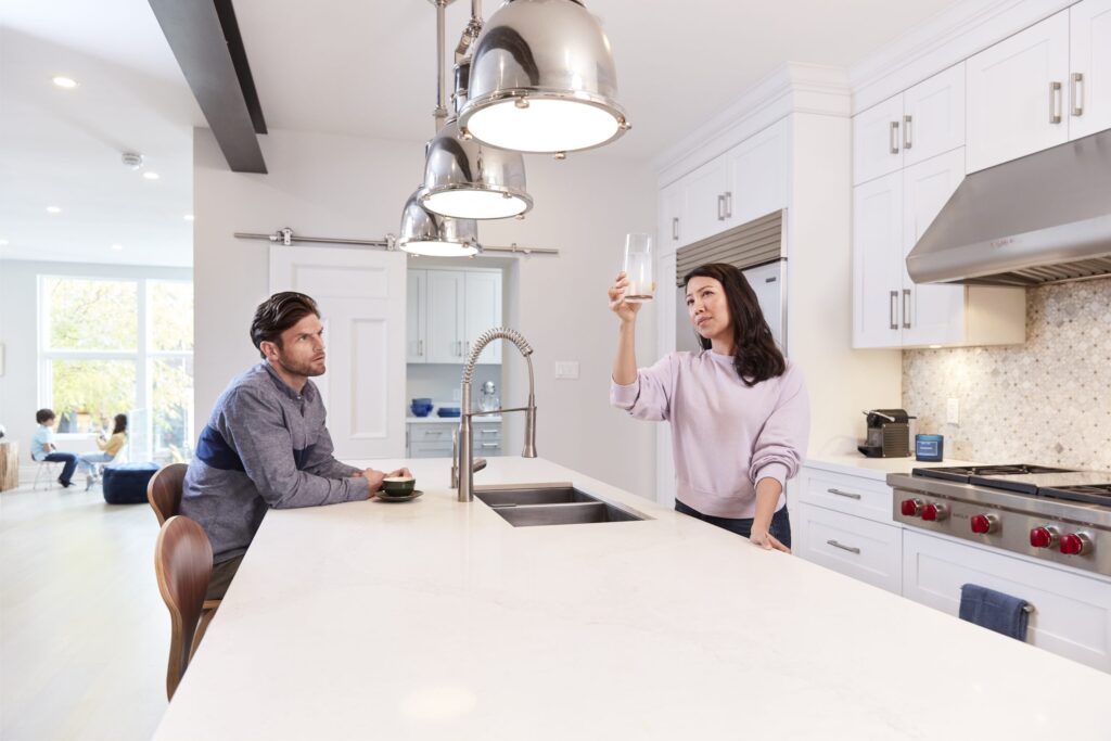 Man and woman sitting at a kitchen island looking at a glass of water from their tap