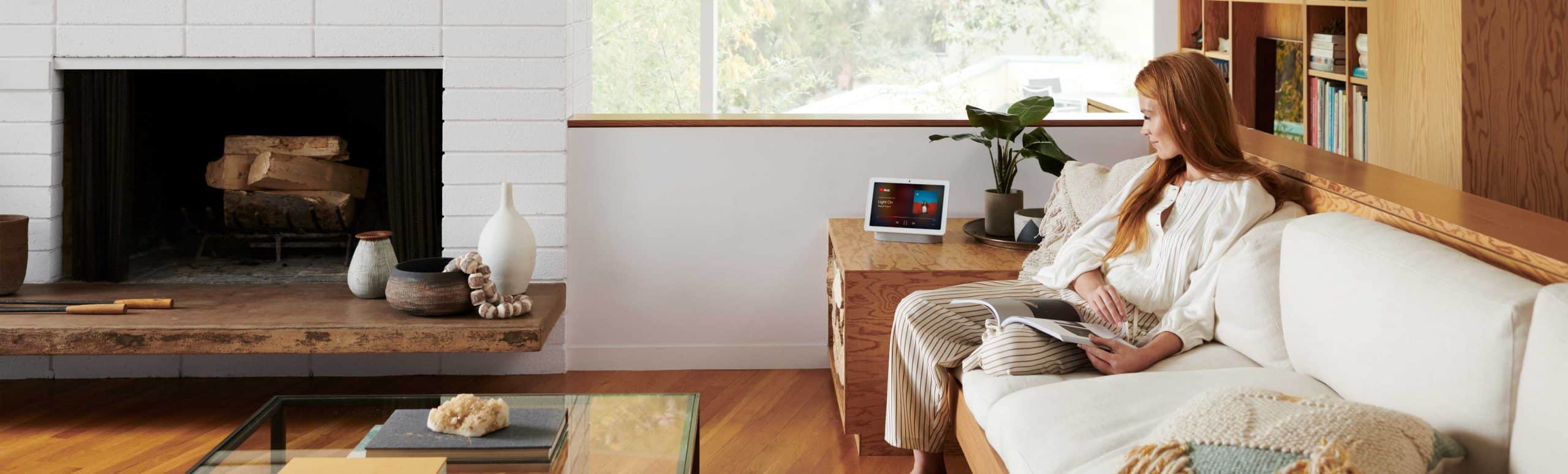 Person sitting on a couch while smiling and looking at a Google Nest Hub