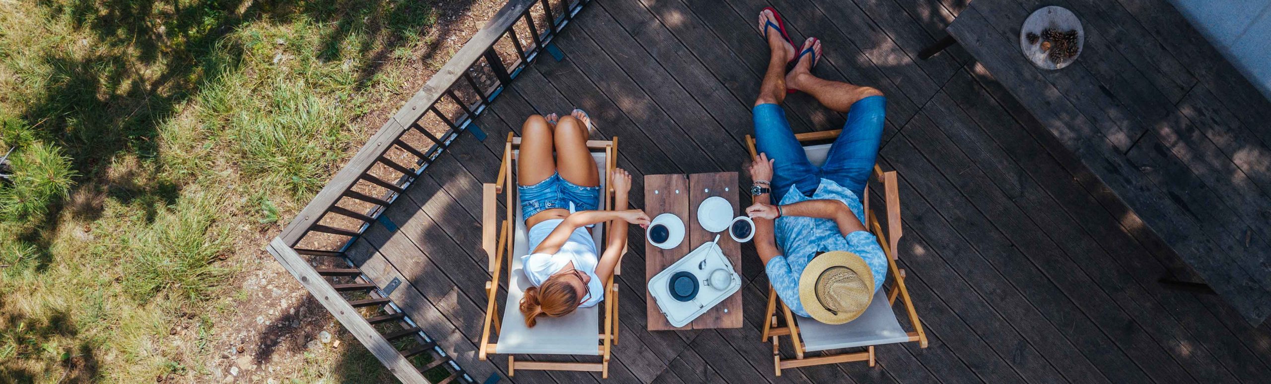 Birds eye view of 2 people sitting outside on a deck with coffee