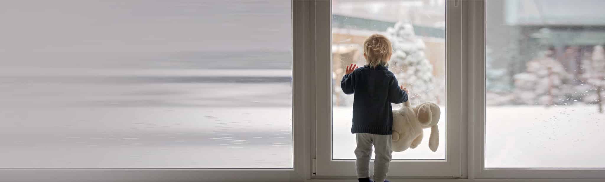 Child holding a stuffed animal looking out the glass windows at the snow