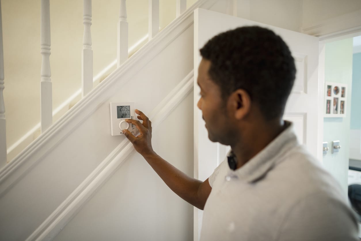A side-view shot of a man turning down a thermostat in his home