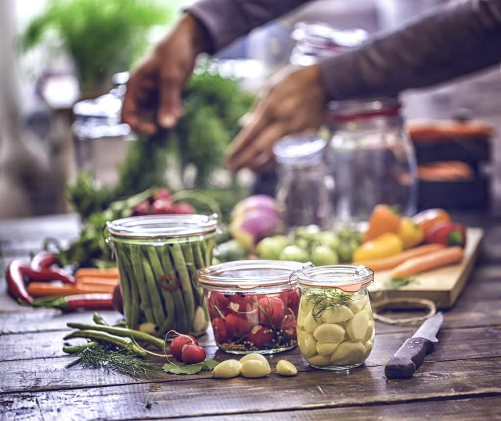 Wooden table with a variety of vegetables on a cutting board and in glass jars