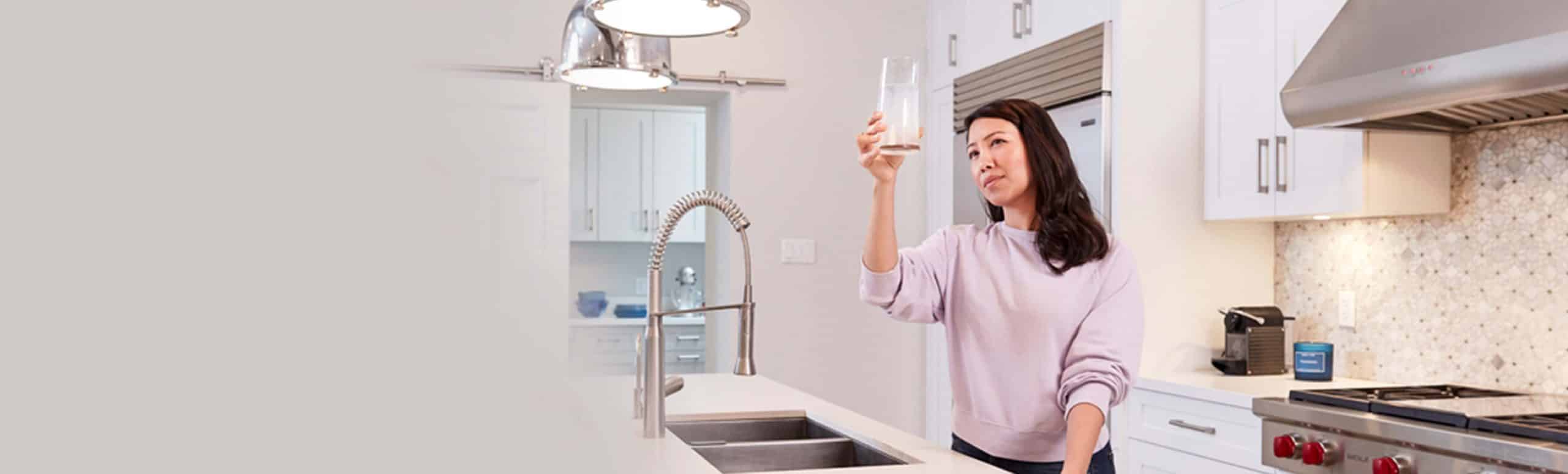 Woman in a kitchen holding up a glass of water and analysing it