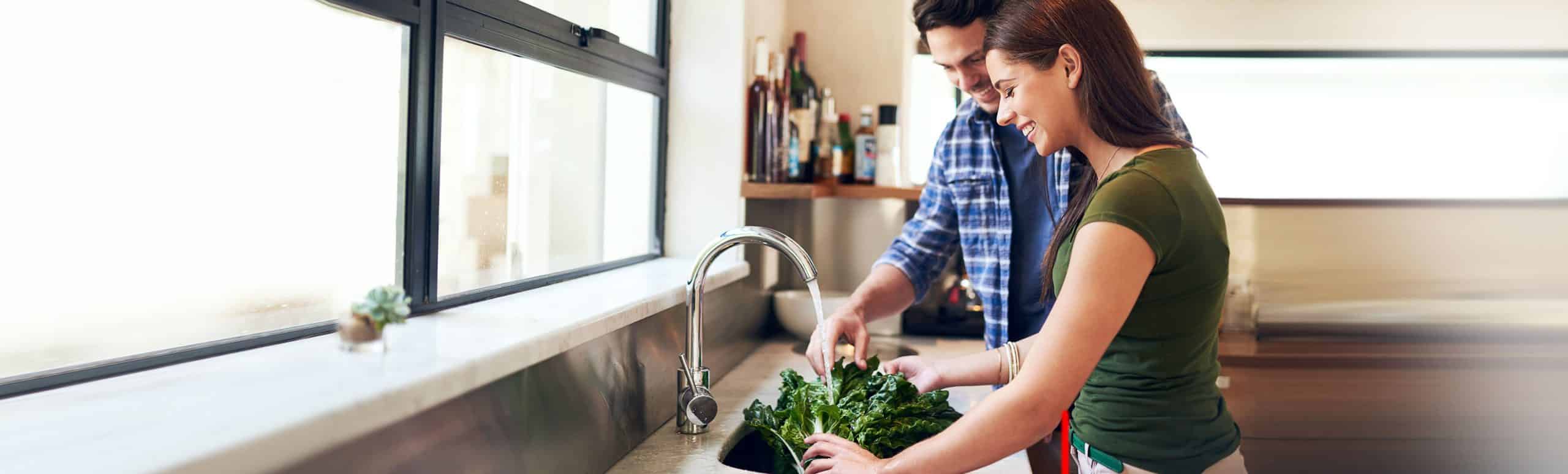 Couple in the kitchen washing lettuce in the sink while smiling together