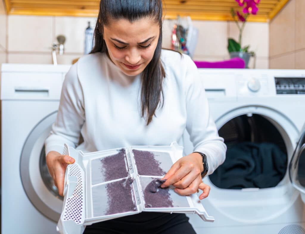 Woman removing lint from fluff dust filter of the tumble dryer