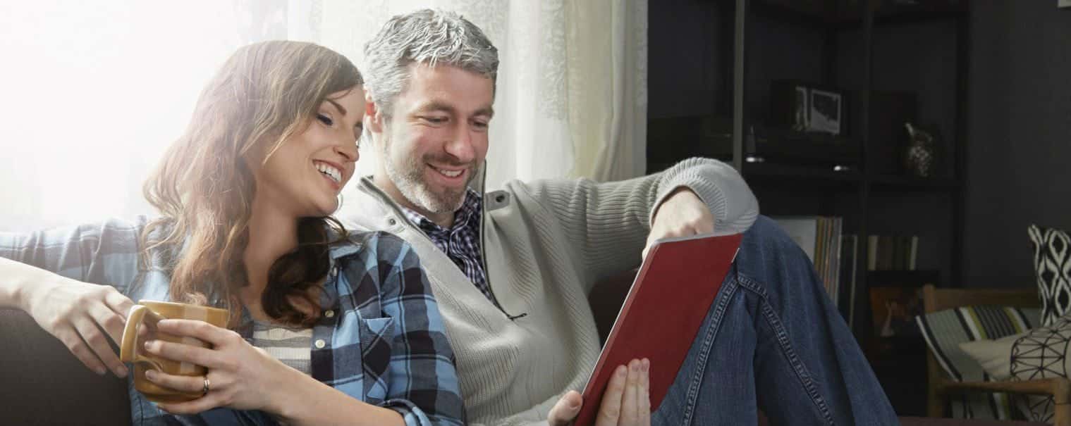 man and woman sitting on a couch looking at their tablet
