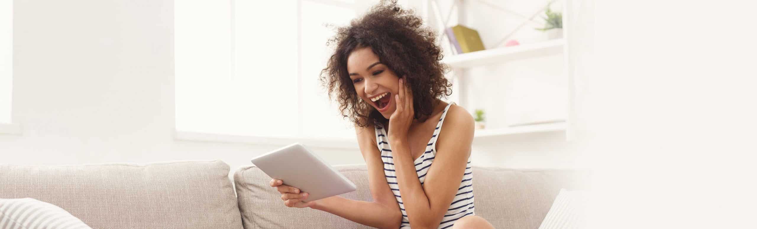 Woman sitting on sofa looking at tablet shocked from offers and rebates