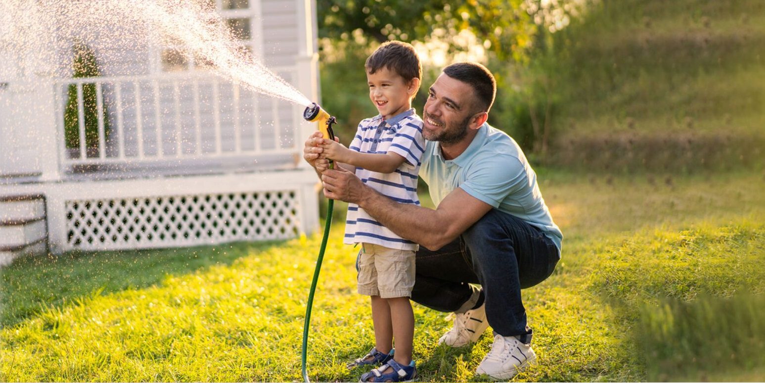 Dad and son watering backyard with hose plumbing
