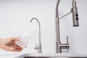 Woman get filtered water from stainless faucet into a glass.