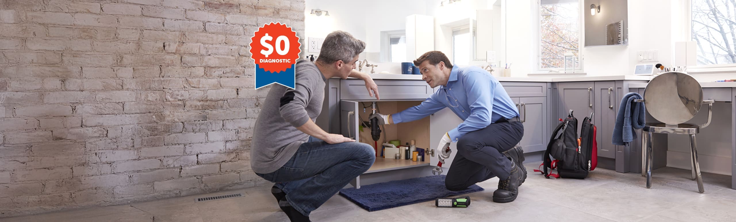 two plumbers kneeling and wokring under a sink