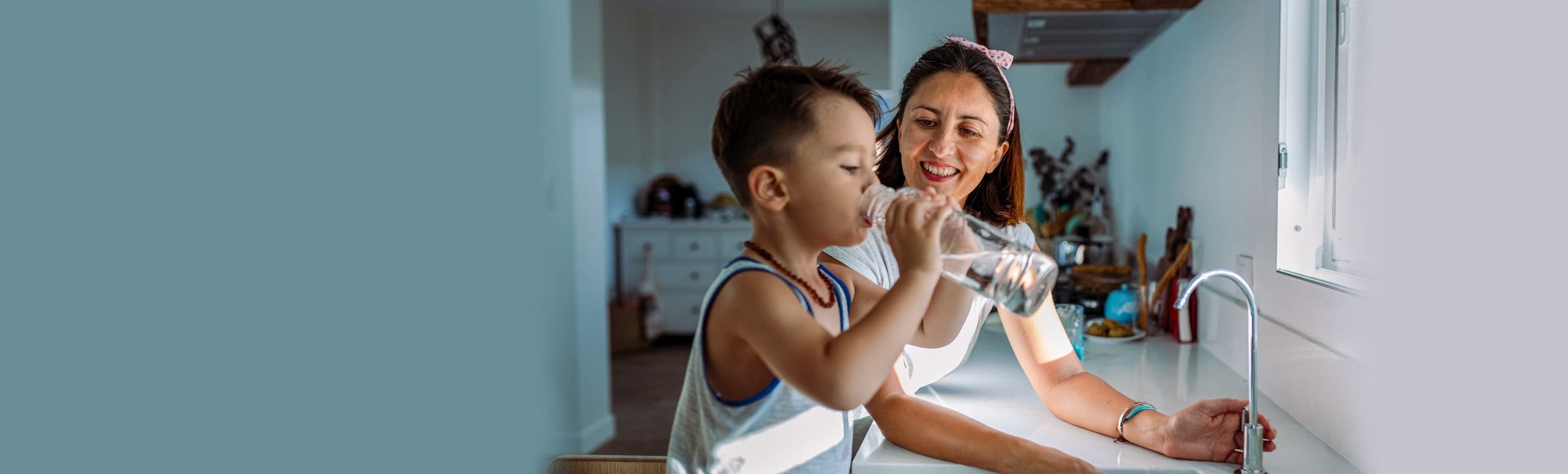 Mother and son drinking at home by the kitchen sink drinking water from a bottle