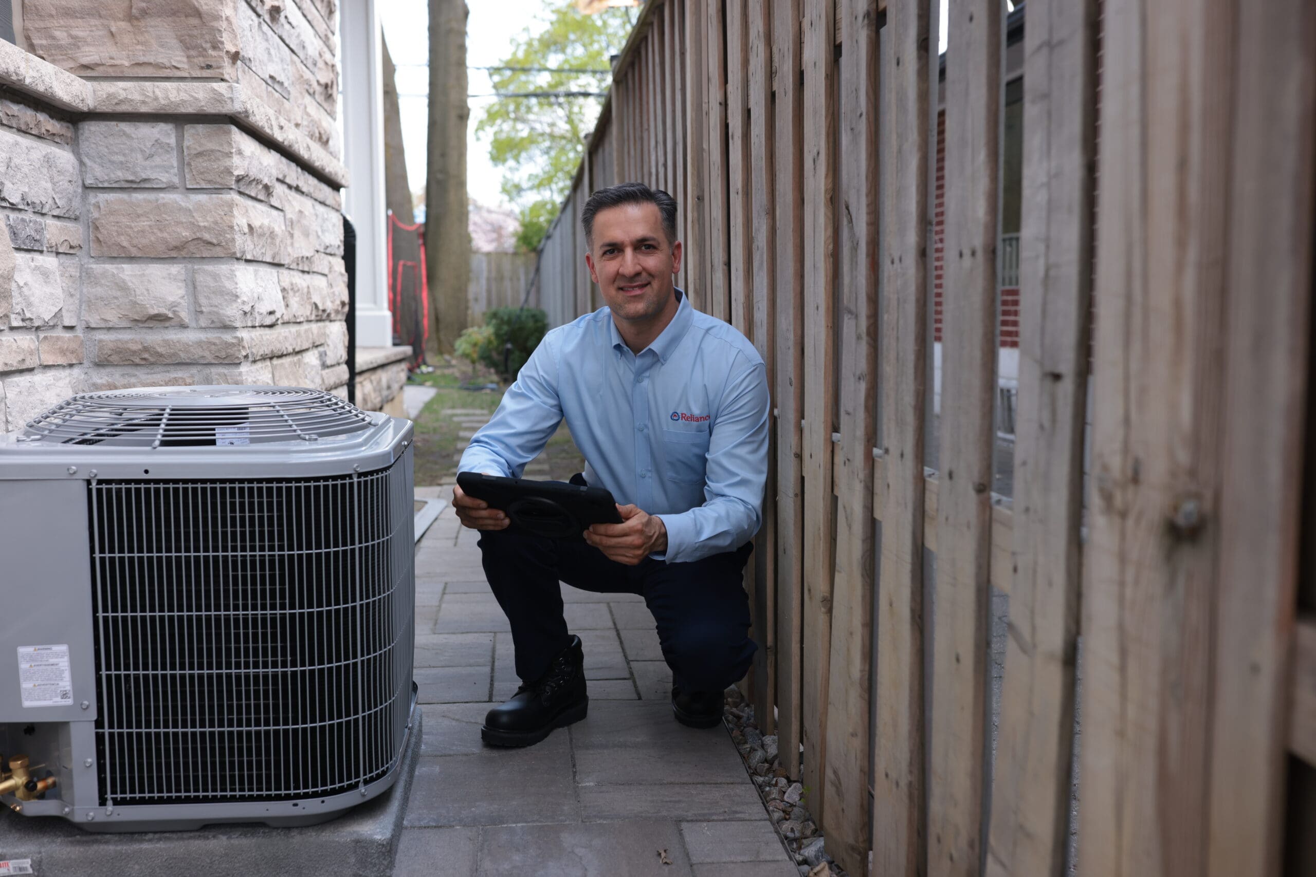 A Reliance technician smiles beside an AC condensor