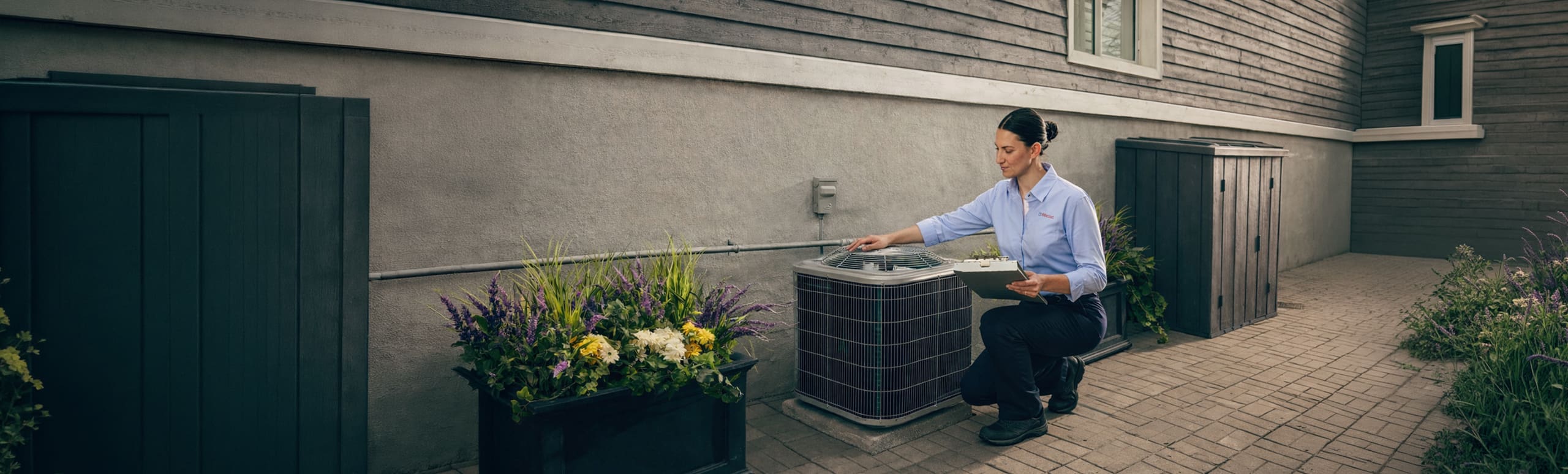 A female Reliance technician inspects an AC condenser outside a home